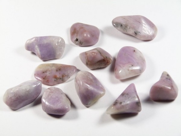 Kilka wygładzonych, fioletowych kamieni leży rozproszonych na białym tle.