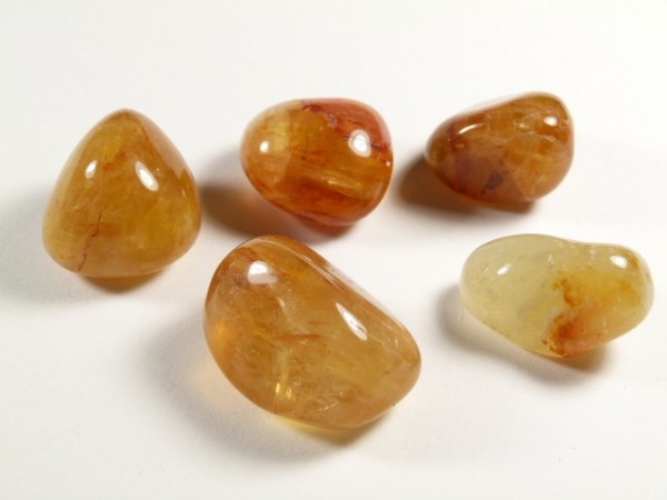 Pięć wypolerowanych, żółtopomarańczowych kamieni leży na białym tle.
