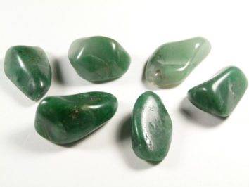 Sześć zielonych, gładkich kamieni leży na białym tle.