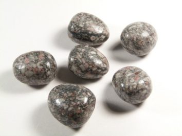 Sześć gładkich, szarych kamieni z różowymi i białymi plamkami na białym tle.