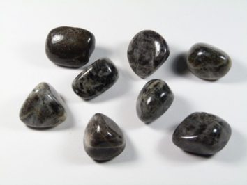 Siedem polerowanych, ciemnych kamieni leży na białym tle.