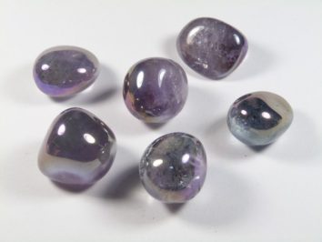 Sześć polerowanych fioletowych kamieni leży na białym tle.