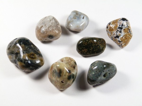 Siedem polerowanych kamieni o różnych kolorach leży na białym tle.