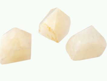 Kalcyt - kamień naturalny, surowy, nieszlifowany. Trzy żółtawe kryształy o geometrycznych kształtach na białym tle.