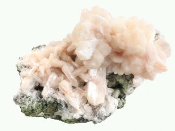 Stilbit - kamień naturalny, surowy, nieszlifowany. Różowy kryształ stilbit na zielono-białej skale, widok z bliska.