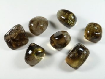 Siedem wypolerowanych, brązowych kamieni leży na białym tle.