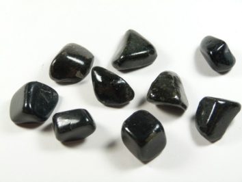 Osiem czarnych, wypolerowanych kamieni leży na białym tle.