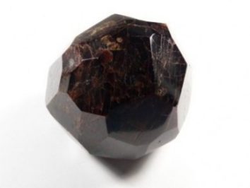 Granat almandyn okaz gładzony. Ciemny, oszlifowany kryształ granatu na białym tle.