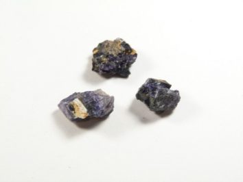 Trzy surowe bryłki ametystu na białym tle.