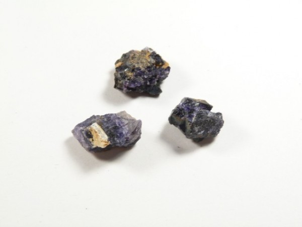Trzy surowe bryłki ametystu na białym tle.