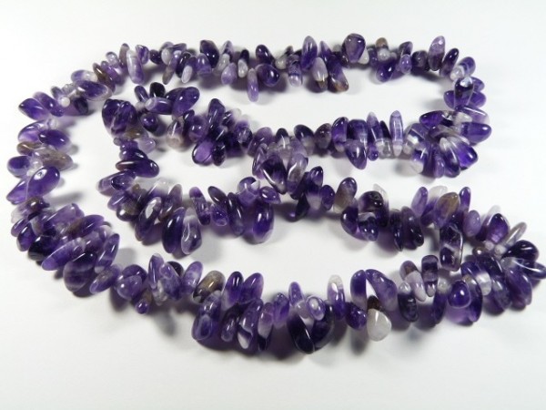 Naszyjnik z nieregularnych, fioletowych kamieni ametystu na białym tle.
