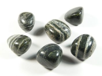 Sześć wypolerowanych, ciemnych kamieni z jasnymi smugami na białym tle.