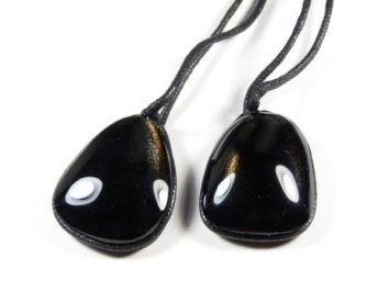 Dwa czarne, gładkie wisiorki z kamienia na czarnych sznurkach, leżące obok siebie.