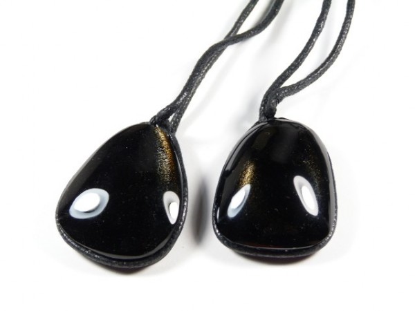 Dwa czarne, gładkie wisiorki z kamienia na czarnych sznurkach, leżące obok siebie.