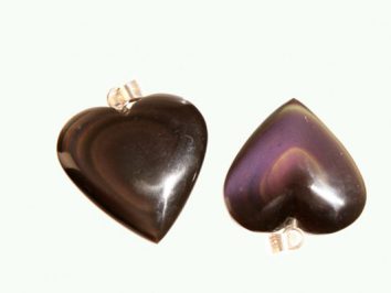 Dwa serca z czarnego kamienia z metalowymi zawieszkami leżą obok siebie na jasnym tle.