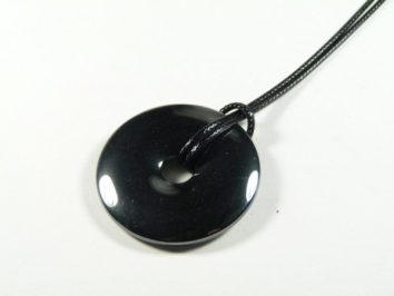 Czarny, okrągły wisiorek z kamienia na czarnym sznurku, leżący na białym tle.