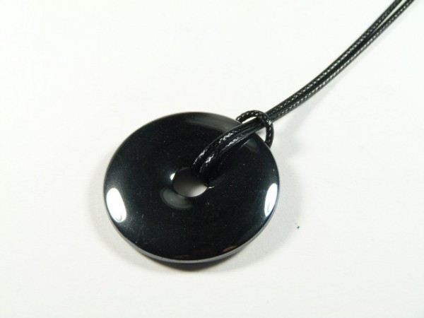 Czarny, okrągły wisiorek z kamienia na czarnym sznurku, leżący na białym tle.
