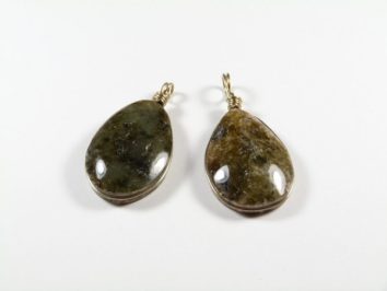 Dwie wiszące zawieszki z kamienia o owalnym kształcie, na białym tle.