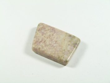 Wypolerowany, prostokątny kamień o jasnoróżowej barwie na białym tle.