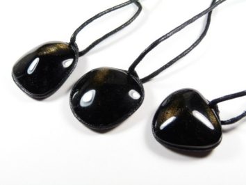 Trzy czarne, błyszczące wisiorki na czarnych sznurkach leżą na białym tle.