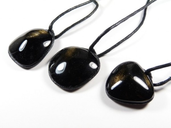 Trzy czarne, błyszczące wisiorki na czarnych sznurkach leżą na białym tle.