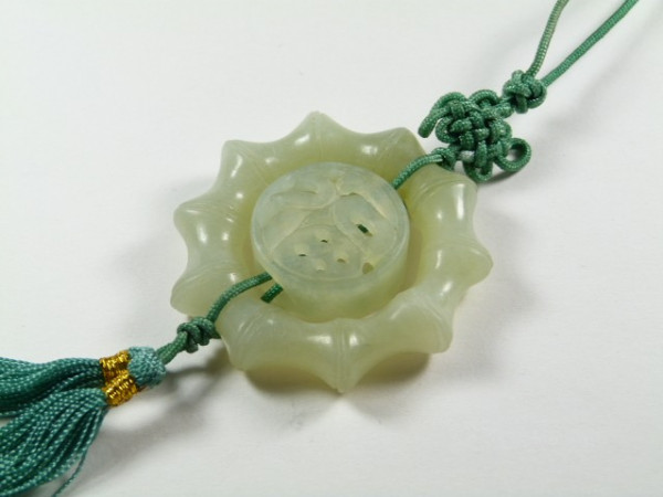 Jasny jadeitowy amulet z zielonym sznurkiem i ozdobnym węzłem leży na białym tle.