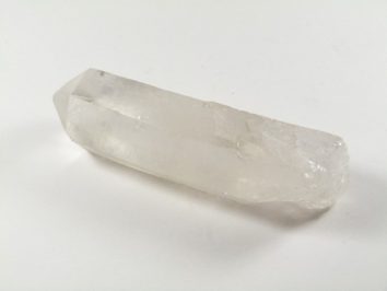 Przezroczysty kryształ kwarcu leży na białym tle.