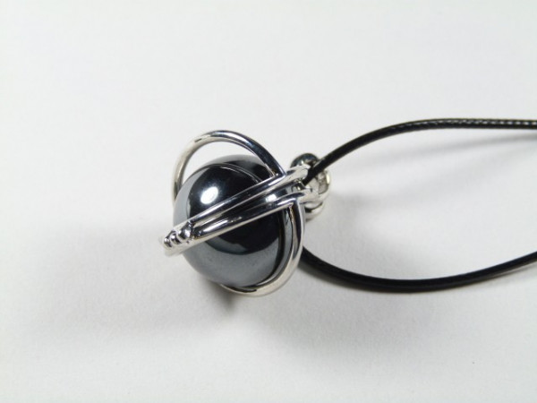 Wisiorek z czarną kulką w srebrnej oprawie na czarnym rzemyku, na białym tle.