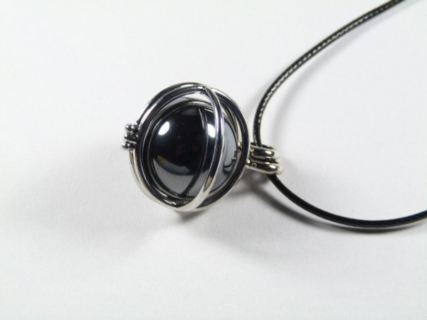 Srebrny naszyjnik z czarną kulką w metalowej oprawie, leżący na białym tle.