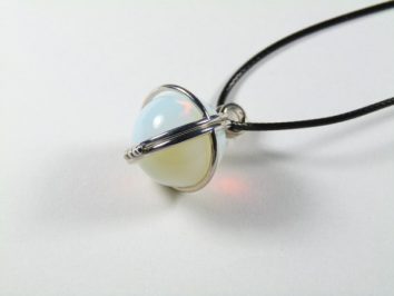 Wisiorek z opalizującą kulką na czarnym sznurku, oprawiony w srebrny metal.