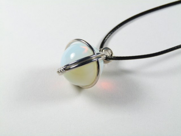 Wisiorek z opalizującą kulką na czarnym sznurku, oprawiony w srebrny metal.