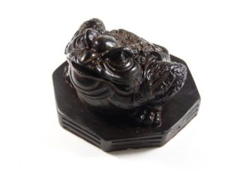 Czarna figurka żaby siedzącej na ośmiokątnej podstawce, widok z góry.