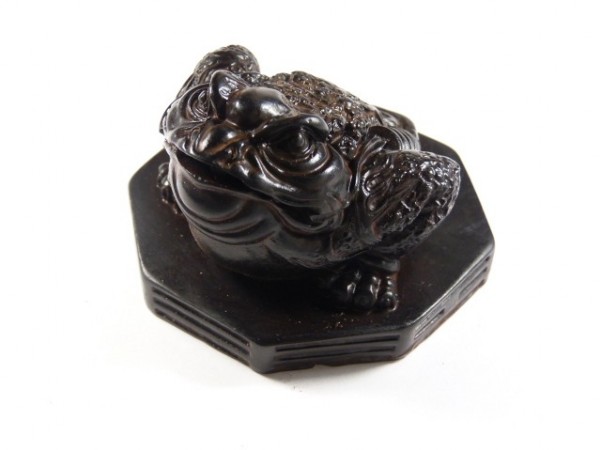 Czarna figurka żaby siedzącej na ośmiokątnej podstawce, widok z góry.