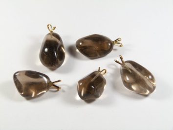 Pięć brązowych, gładkich kamieni z metalowymi zawieszkami na białym tle.