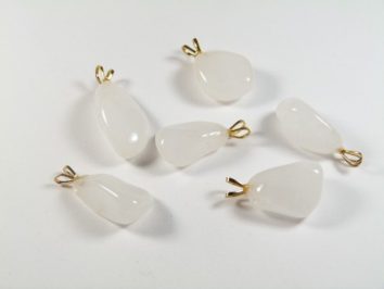 Sześć białych, opalizujących zawieszek z kamieniami i złotymi uchwytami, leżących na białym tle.