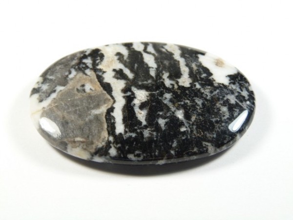 Jaspis zebra - kamień gładzony, polerowany, szlifowany. Wypolerowany, owalny kamień z czarno-białym, pasiastym wzorem na białym tle.