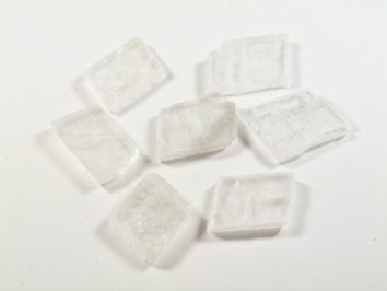 Spar islandzki - kamień naturalny, surowy, nieszlifowany. Siedem białych kryształków na białym tle.