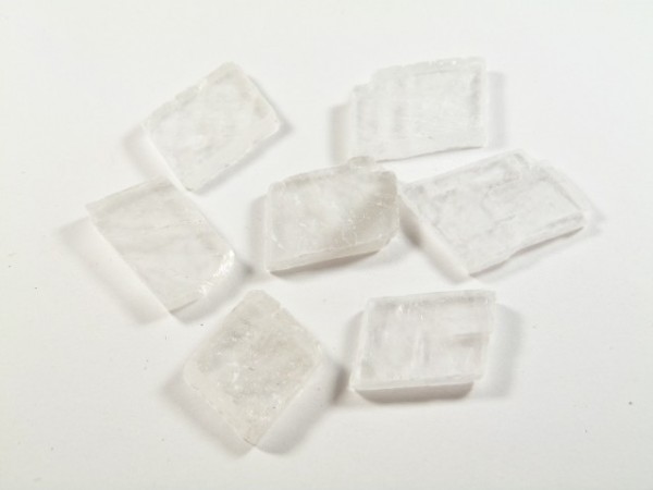 Spar islandzki - kamień naturalny, surowy, nieszlifowany. Siedem białych kryształków na białym tle.