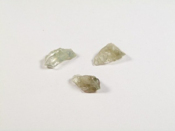 Prasiolit/ prazjolit - kamień gładzony, polerowany. Trzy niewielkie, przezroczyste kamienie prasiolit/ prazjolit szkła leżące na białym tle.