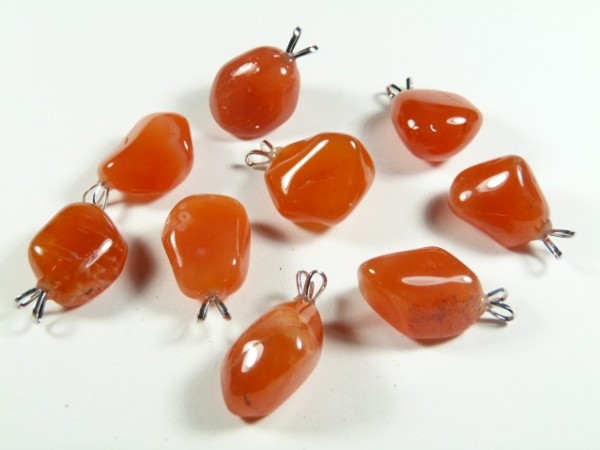 Osiem polerowanych wisiorków z karneolu na białym tle.
