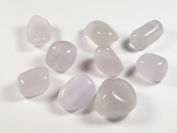 Fluoryt liliowy - kamień gładzony, polerowany, szlifowany i bębnowany w formie otoczaka. Dziewięć gładkich, mlecznobiałych kamieni leży na białym tle.