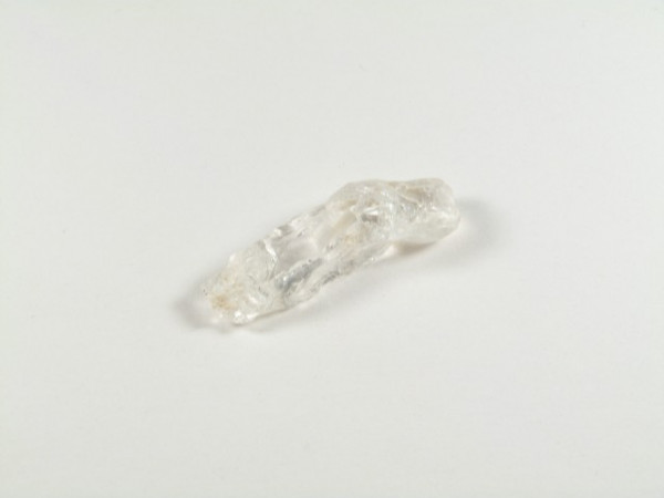 Przezroczysty kryształ górski leży na białym tle.