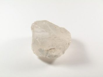 Przezroczysty, nieregularny kryształ kwarcu leży na białym tle.