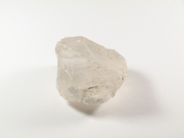 Przezroczysty, nieregularny kryształ kwarcu leży na białym tle.