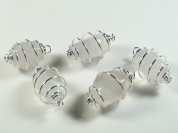 Pięć białych koralików owiniętych srebrnym drutem leży na białym tle.