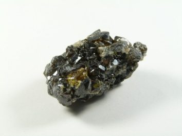 Sfaleryt - kamień naturalny, surowy, nieszlifowany. Kawałek ciemnego, błyszczącego minerału o nieregularnych kształtach na białym tle.