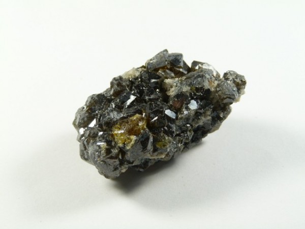 Sfaleryt - kamień naturalny, surowy, nieszlifowany. Kawałek ciemnego, błyszczącego minerału o nieregularnych kształtach na białym tle.