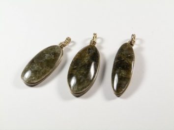 Trzy owalne wisiorki z ciemnego kamienia na białym tle.