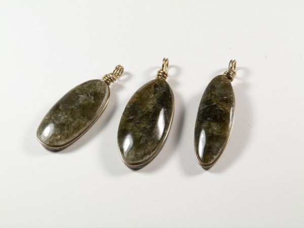 Trzy owalne wisiorki z ciemnego kamienia na białym tle.