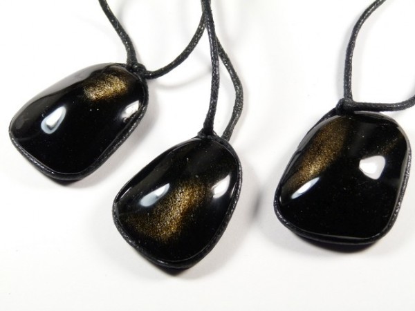 Trzy czarne kamienie z połyskiem na czarnych sznurkach, ułożone na białym tle.